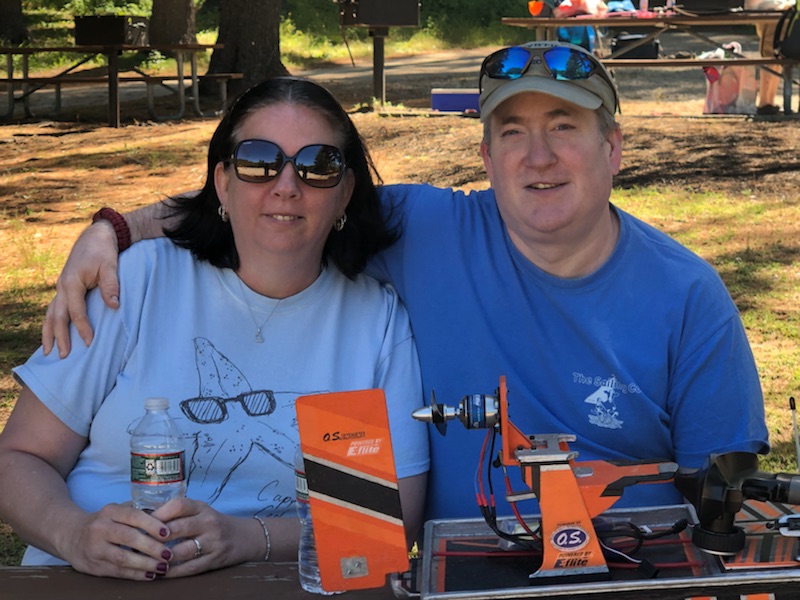 A smiling male and female smiling with sunglasses and blue shirts. They are sitting in front of an orange tool.